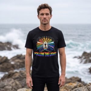 Man on a rocky coastline wearing a black tee printed with a white lighthouse firing rays of every color, above Follow The Light in rainbow capitals