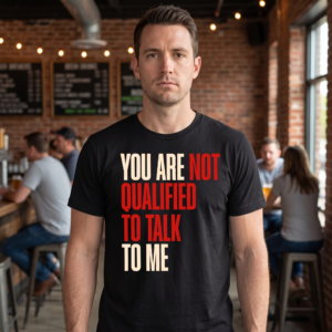 Man wearing a black tee in a taproom, printed with four lines of heavy capitals alternating cream and red, reading You are not qualified to talk to me